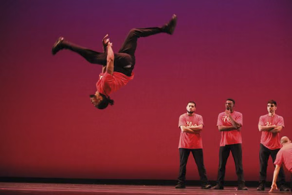 FLY Dance Company performers mid-routine, showcasing their signature 'theatrical hip hop' style with high-energy street dance moves.