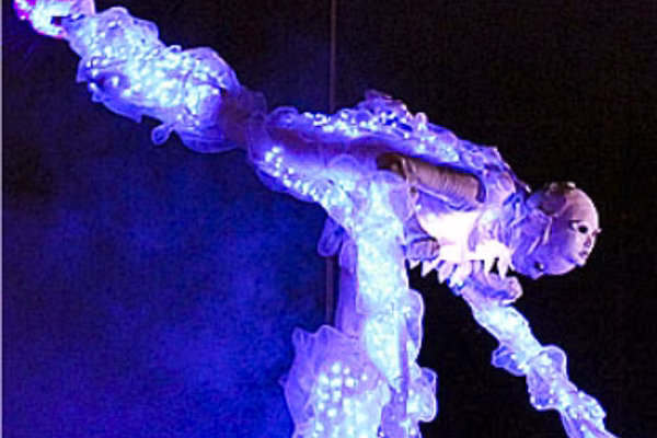 Light Beings Illuminated Stilt Walkers glowing in vibrant LED costumes, towering above the crowd with ethereal, futuristic elegance.